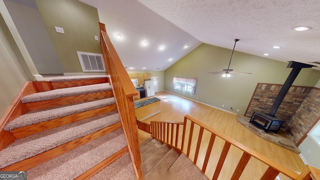 staircase with wood-type flooring, a wood stove, a textured ceiling, high vaulted ceiling, and ceiling fan