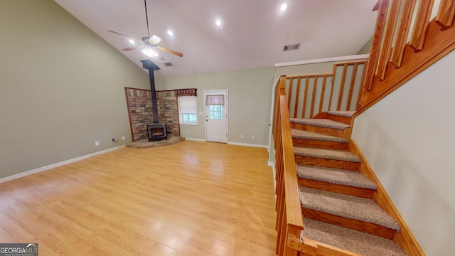 unfurnished living room with a wood stove, high vaulted ceiling, light hardwood / wood-style floors, and ceiling fan