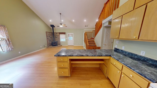 kitchen with kitchen peninsula, dark stone counters, ceiling fan, a wood stove, and light wood-type flooring