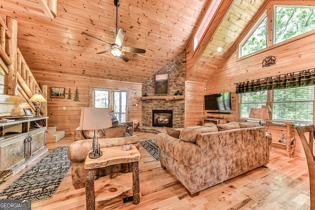 living room with wood walls, wooden ceiling, high vaulted ceiling, a stone fireplace, and light hardwood / wood-style flooring