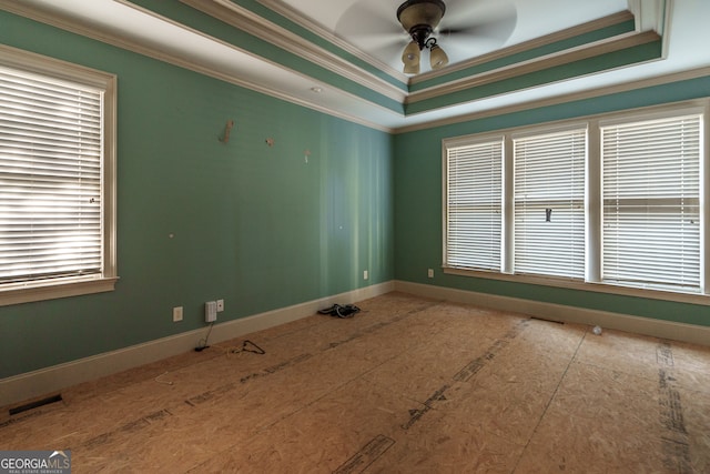 empty room featuring a tray ceiling, a wealth of natural light, and ornamental molding