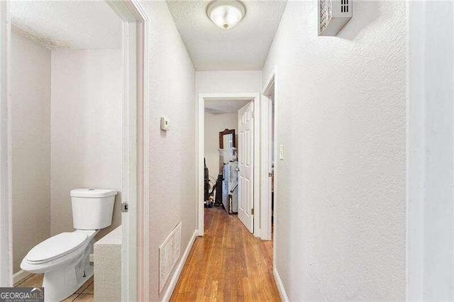 hallway with a textured ceiling and light hardwood / wood-style flooring