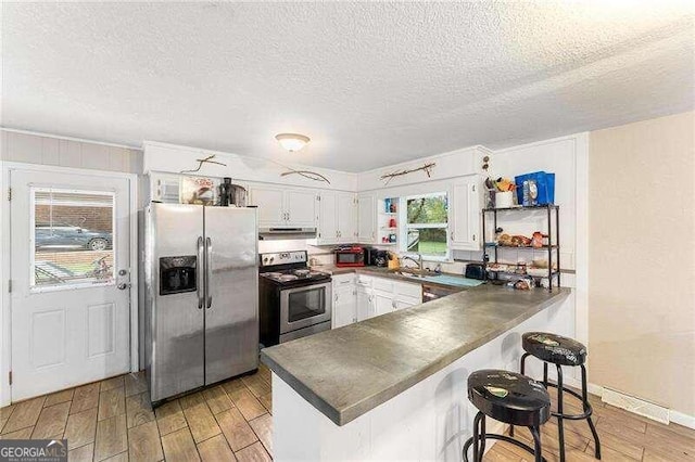 kitchen with white cabinets, a textured ceiling, light hardwood / wood-style flooring, and appliances with stainless steel finishes