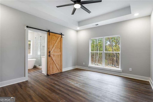 empty room with a raised ceiling, a barn door, ceiling fan, and dark wood-type flooring