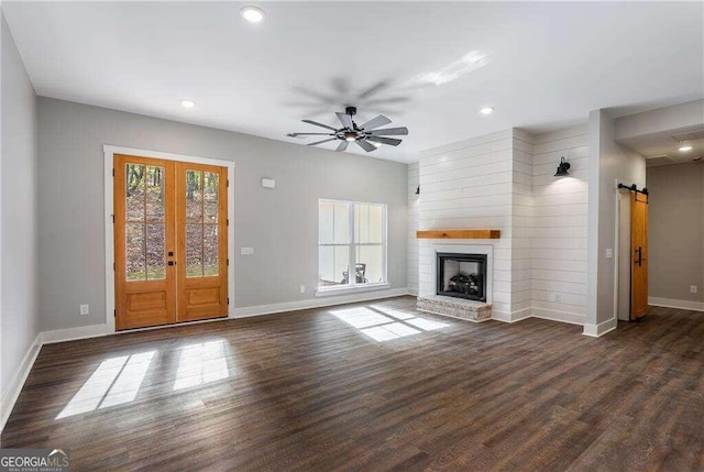 unfurnished living room with french doors, a brick fireplace, dark hardwood / wood-style floors, a barn door, and ceiling fan