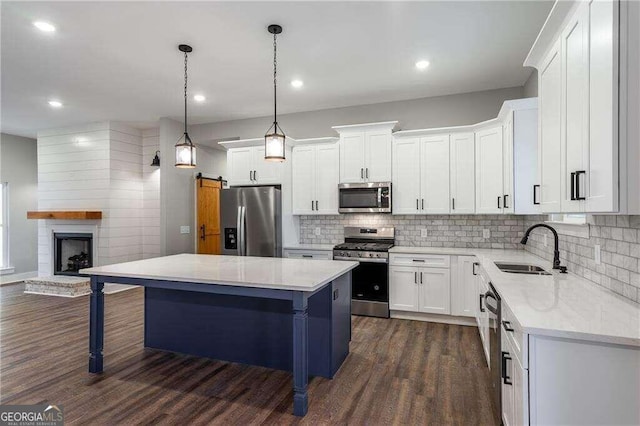 kitchen featuring white cabinetry, sink, a fireplace, a kitchen island, and appliances with stainless steel finishes