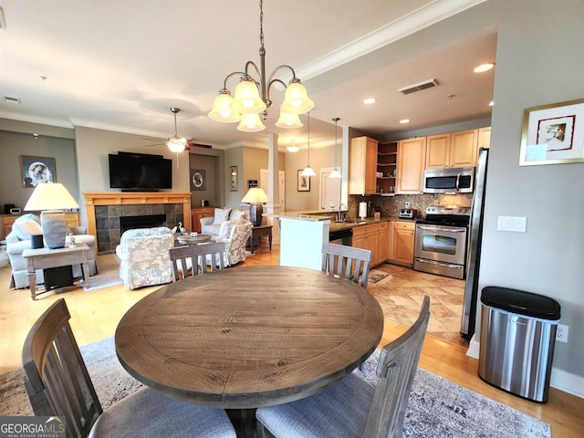 dining space with a tiled fireplace, sink, light hardwood / wood-style flooring, and ceiling fan with notable chandelier