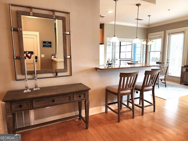 bar with ornamental molding, light hardwood / wood-style flooring, and hanging light fixtures