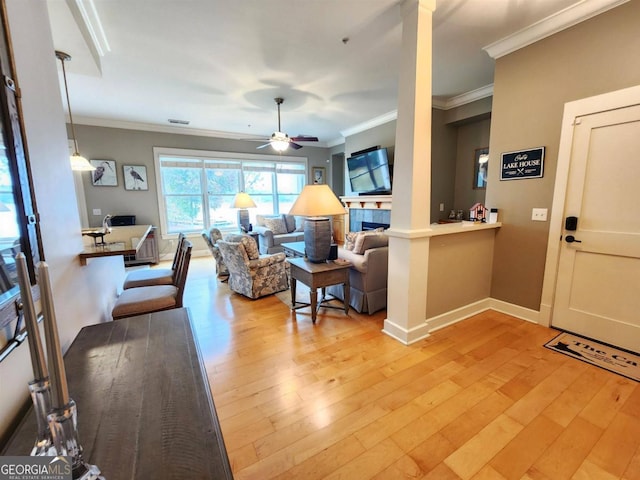 living room with light hardwood / wood-style floors, ceiling fan, a tiled fireplace, and ornamental molding