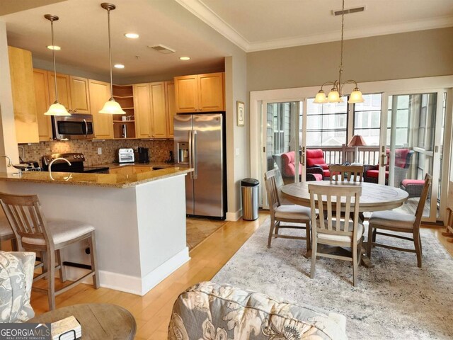 kitchen with light stone counters, kitchen peninsula, light wood-type flooring, appliances with stainless steel finishes, and decorative light fixtures