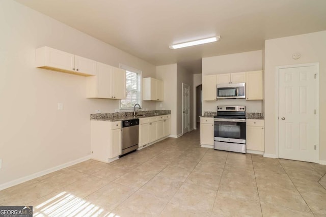 kitchen featuring stainless steel appliances, dark stone counters, light tile patterned floors, sink, and white cabinets