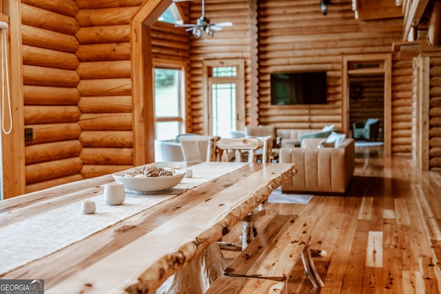 unfurnished dining area featuring hardwood / wood-style flooring, ceiling fan, and log walls