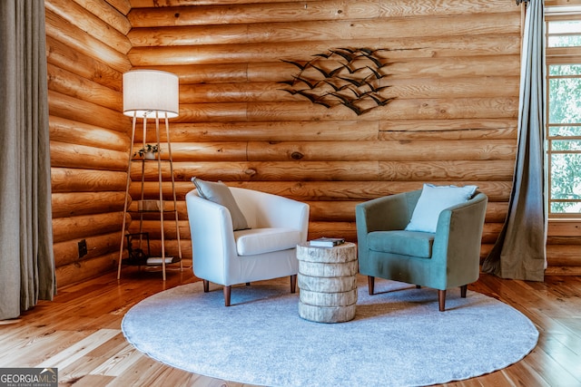 living area with a wealth of natural light, hardwood / wood-style flooring, and log walls