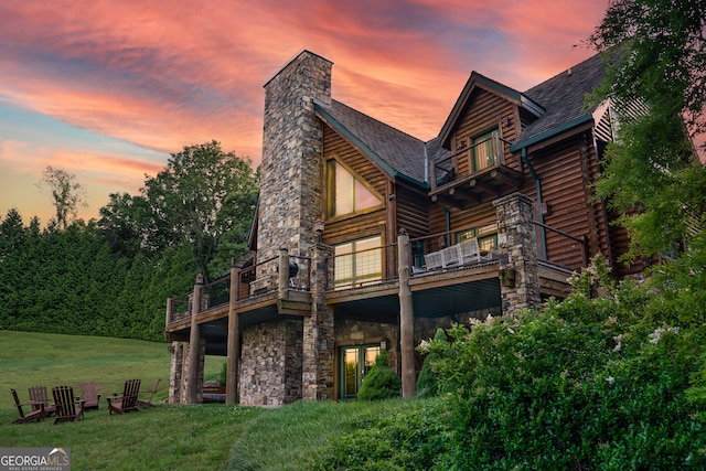 back house at dusk with a lawn and a balcony