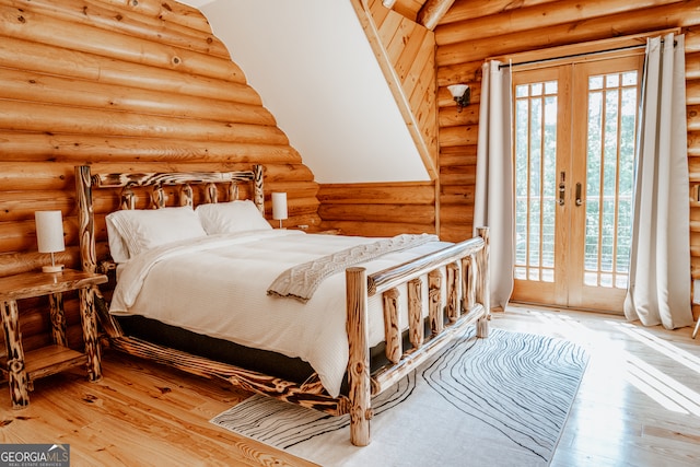 bedroom featuring wood-type flooring, rustic walls, and french doors