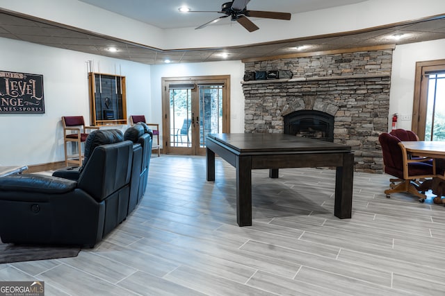 game room featuring ceiling fan, a wealth of natural light, a stone fireplace, and light wood-type flooring