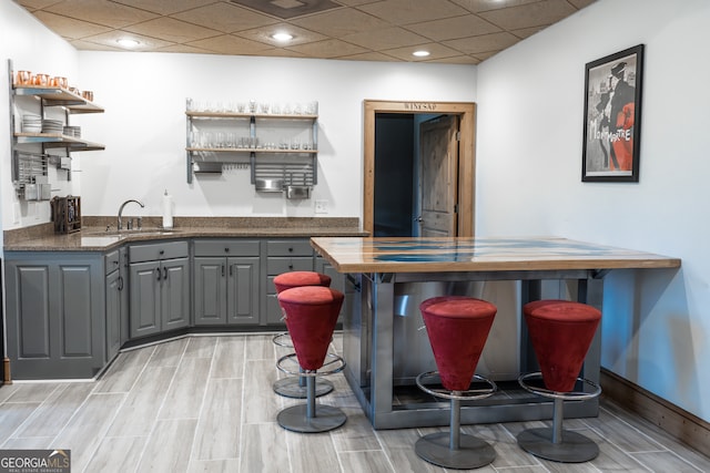 bar featuring gray cabinets, a paneled ceiling, sink, and light hardwood / wood-style floors