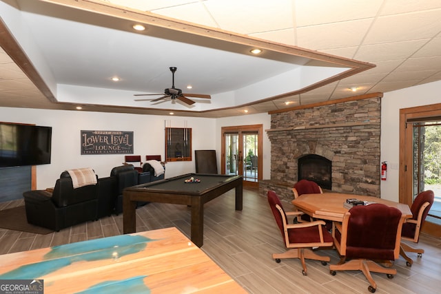 rec room featuring ceiling fan, a tray ceiling, a fireplace, wood-type flooring, and billiards