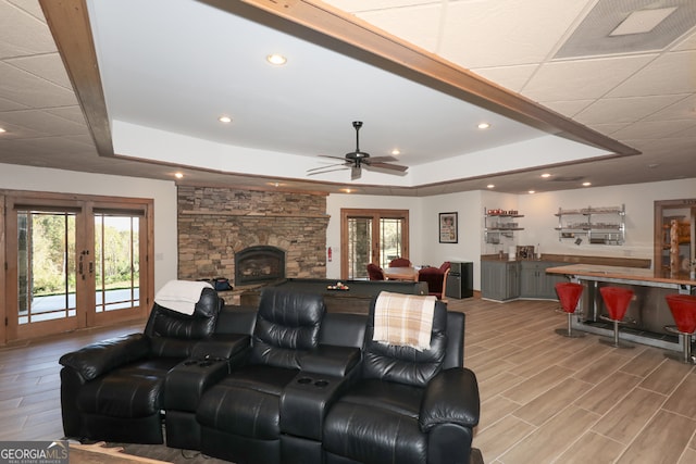 living room with french doors, a fireplace, a raised ceiling, ceiling fan, and light hardwood / wood-style flooring