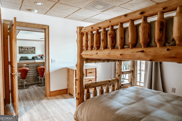 bedroom with light wood-type flooring, a paneled ceiling, and indoor bar