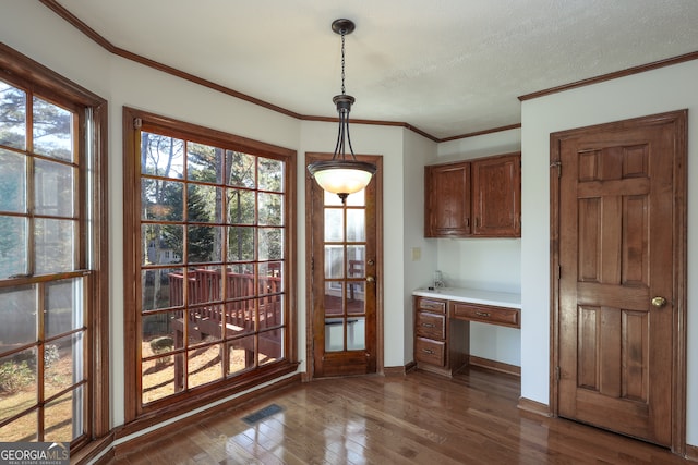 unfurnished dining area with dark hardwood / wood-style flooring, built in desk, a textured ceiling, and crown molding