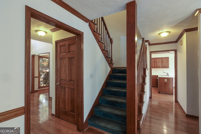 stairway featuring sink, wood-type flooring, a textured ceiling, and ornamental molding