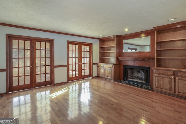 unfurnished living room with french doors, a textured ceiling, a tiled fireplace, hardwood / wood-style flooring, and ornamental molding