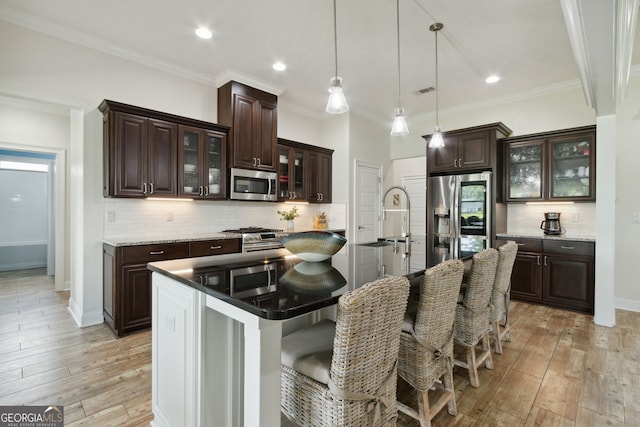 kitchen with dark brown cabinetry, appliances with stainless steel finishes, an island with sink, and light hardwood / wood-style flooring