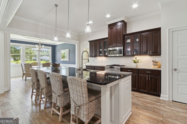 kitchen with stainless steel appliances, hanging light fixtures, a center island with sink, and light wood-type flooring