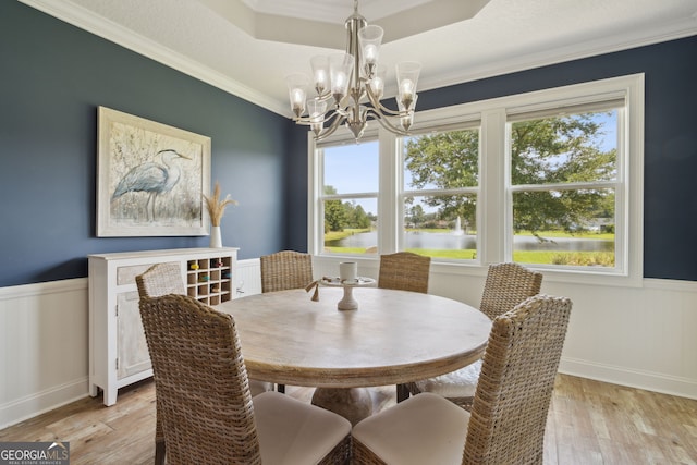 dining room featuring a water view, a chandelier, ornamental molding, a tray ceiling, and light wood-type flooring