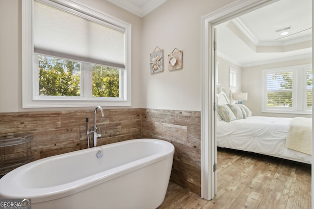 bathroom with ornamental molding, wood-type flooring, a healthy amount of sunlight, and a tub to relax in