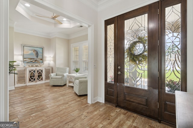 foyer entrance with ceiling fan, a tray ceiling, light hardwood / wood-style floors, and crown molding