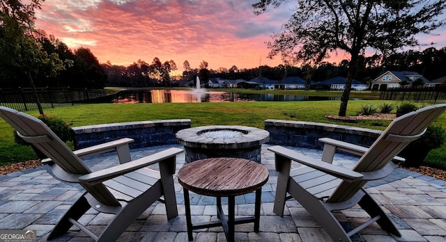 patio terrace at dusk featuring a lawn, a water view, and a fire pit