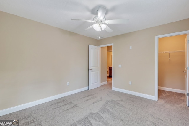 unfurnished bedroom featuring ceiling fan, light carpet, a closet, and a spacious closet