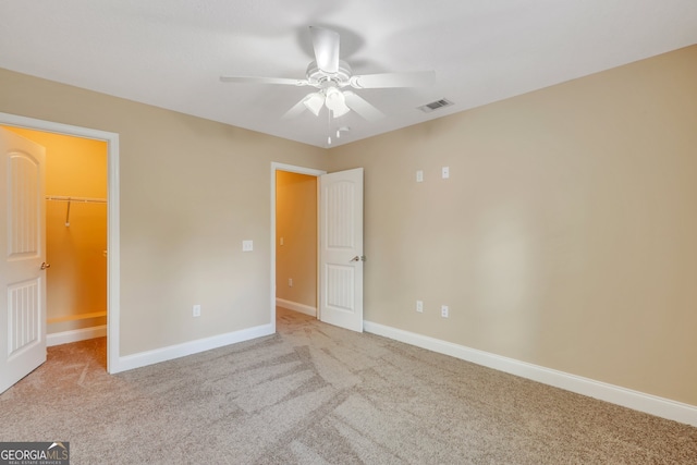 unfurnished bedroom featuring ceiling fan, light carpet, a closet, and a walk in closet