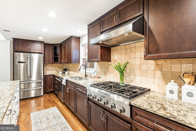 kitchen featuring light stone countertops, sink, backsplash, light hardwood / wood-style floors, and appliances with stainless steel finishes