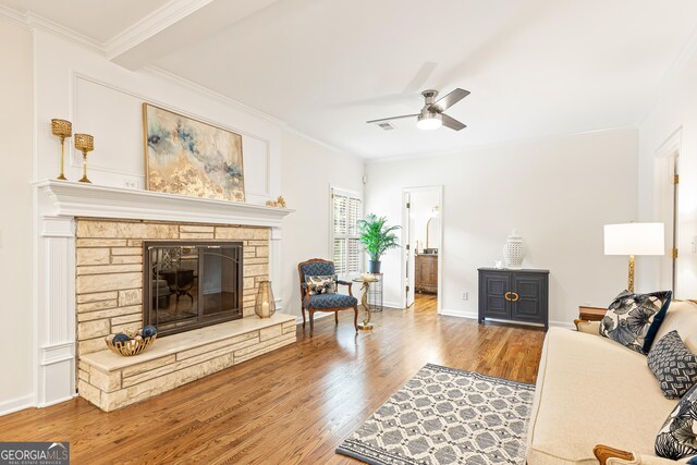 living room with wood-type flooring, a stone fireplace, ceiling fan, and ornamental molding