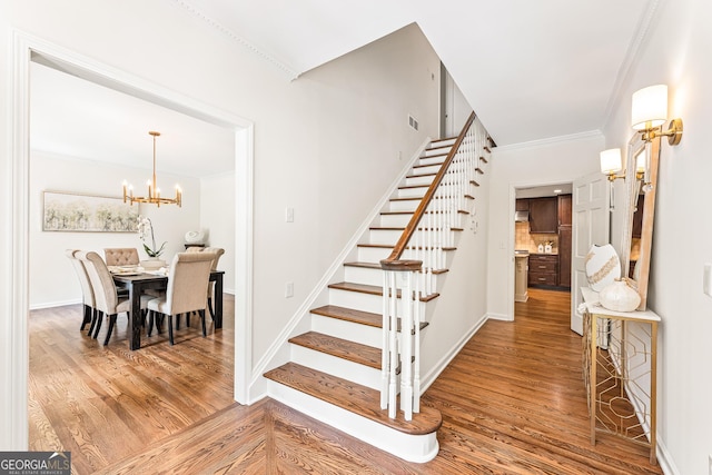 stairs featuring wood-type flooring, crown molding, and an inviting chandelier