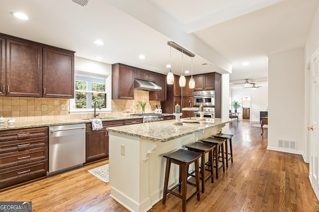 kitchen featuring ceiling fan, light stone counters, decorative light fixtures, a kitchen island, and appliances with stainless steel finishes