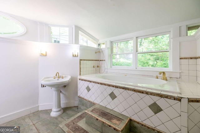 bathroom featuring a relaxing tiled tub, vaulted ceiling, and tile patterned flooring