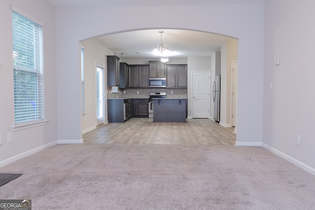 kitchen with appliances with stainless steel finishes, decorative light fixtures, tasteful backsplash, and light colored carpet