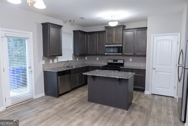 kitchen with stainless steel appliances, sink, light stone countertops, a center island, and light wood-type flooring