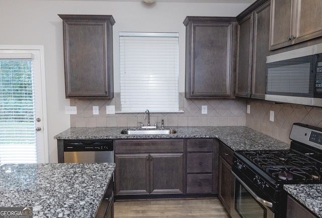 kitchen with stainless steel appliances, dark stone counters, sink, and light hardwood / wood-style flooring