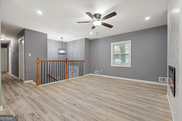 spare room featuring a fireplace, ceiling fan with notable chandelier, and light wood-type flooring