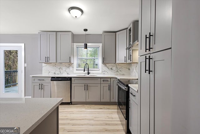 kitchen with appliances with stainless steel finishes, decorative light fixtures, light stone countertops, sink, and light hardwood / wood-style flooring