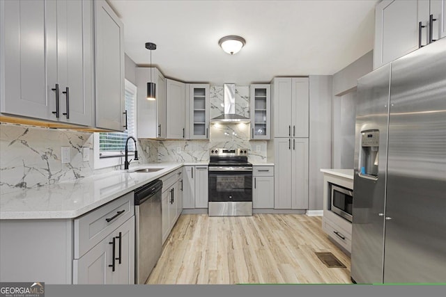 kitchen with stainless steel appliances, wall chimney exhaust hood, decorative light fixtures, light hardwood / wood-style flooring, and gray cabinetry