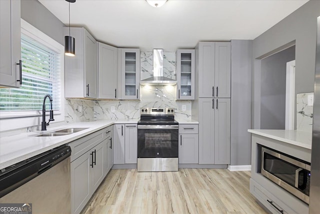 kitchen with stainless steel appliances, wall chimney exhaust hood, sink, pendant lighting, and light wood-type flooring