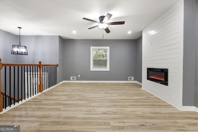 unfurnished living room featuring a fireplace, ceiling fan with notable chandelier, and light wood-type flooring