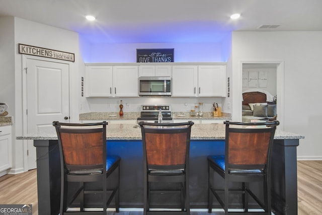 kitchen with stainless steel appliances, light hardwood / wood-style floors, a center island, a breakfast bar area, and white cabinetry