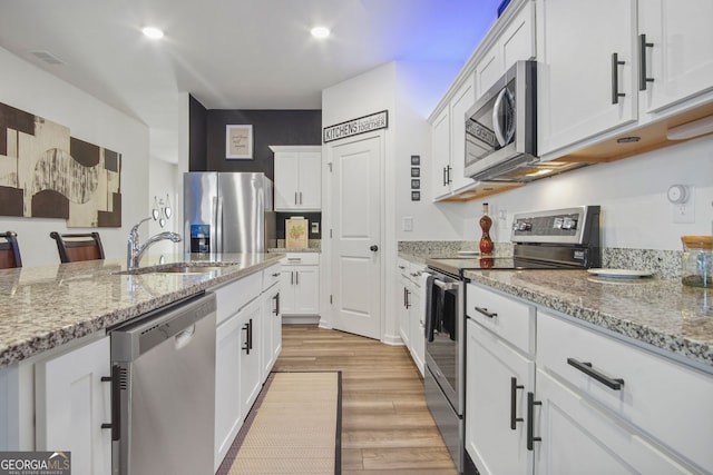 kitchen featuring appliances with stainless steel finishes, light stone countertops, sink, light hardwood / wood-style floors, and white cabinets